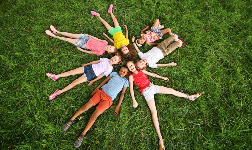 children of different races and nationalities lie on the grass in colorful clothes and smile.