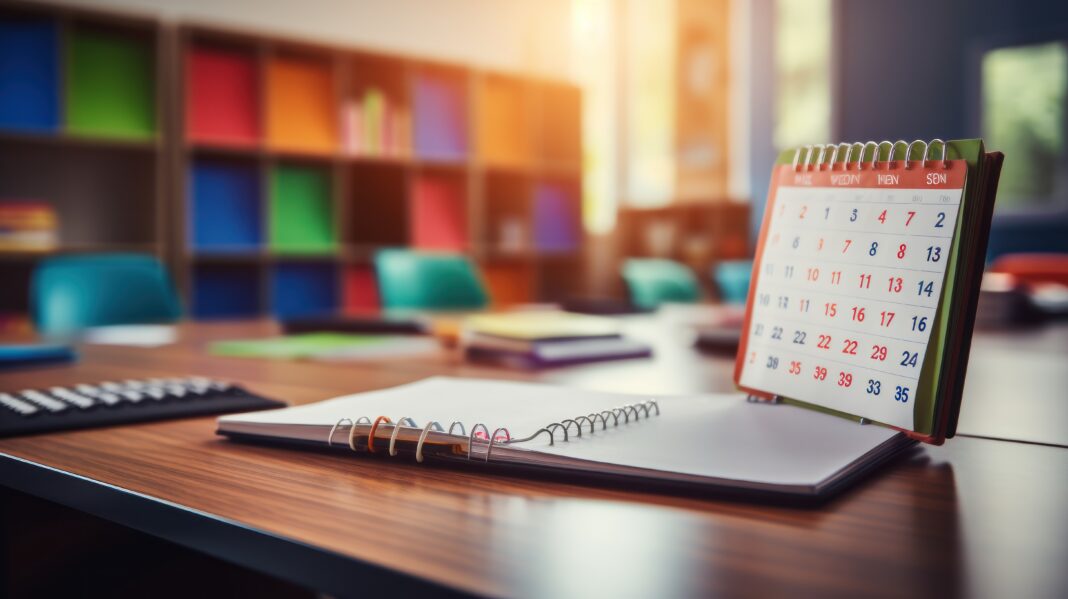 A teacher's desk calendar with important dates highlighted, seen in close-up within an empty classroom.