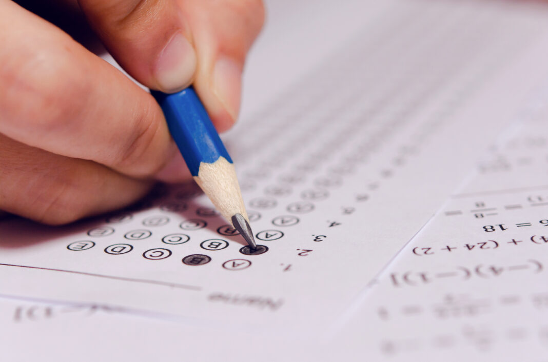 Students hand holding pencil writing selected choice on answer s