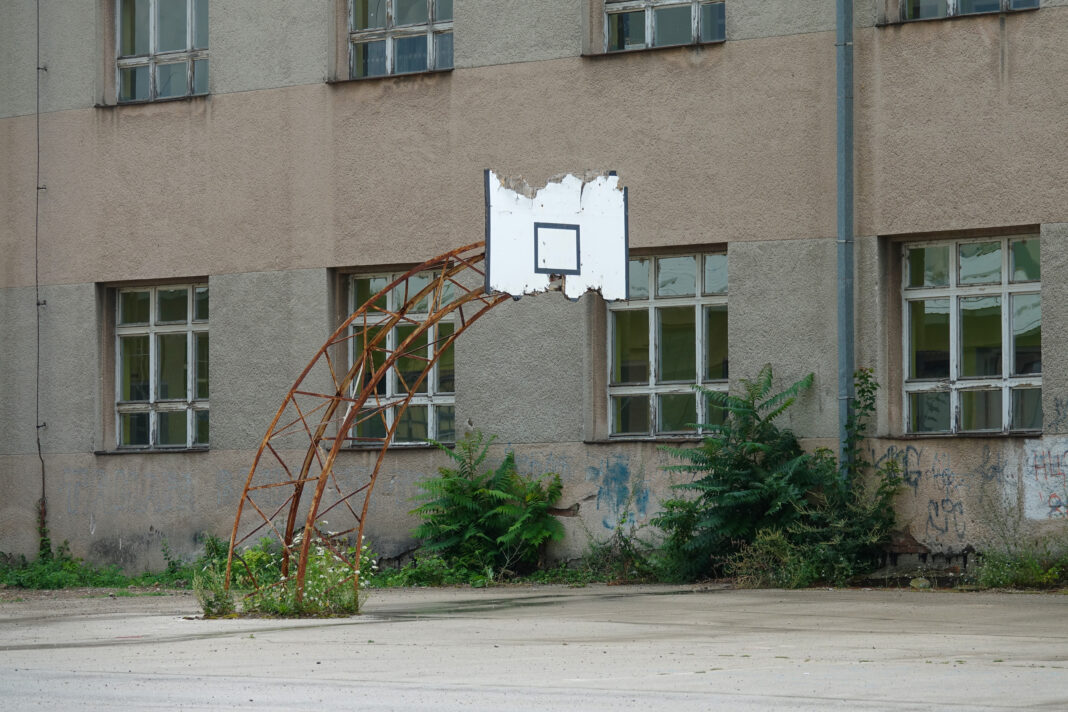 Old basketball hoop is slowly decaying behind old abandoned apartment building.