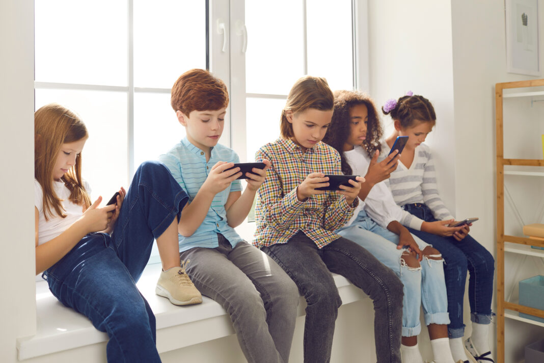 Children sitting on windowsill, playing online games on mobile phones and ignoring each other