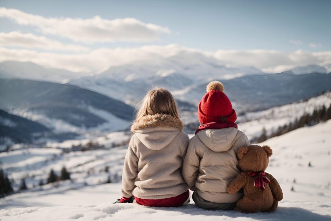 Back view child sits with toy teddy bear and looks at the winter snowy mountains.Winter family vacantion. Christmas celebration and winter holidays. Winter fun and outdoor activities with kids