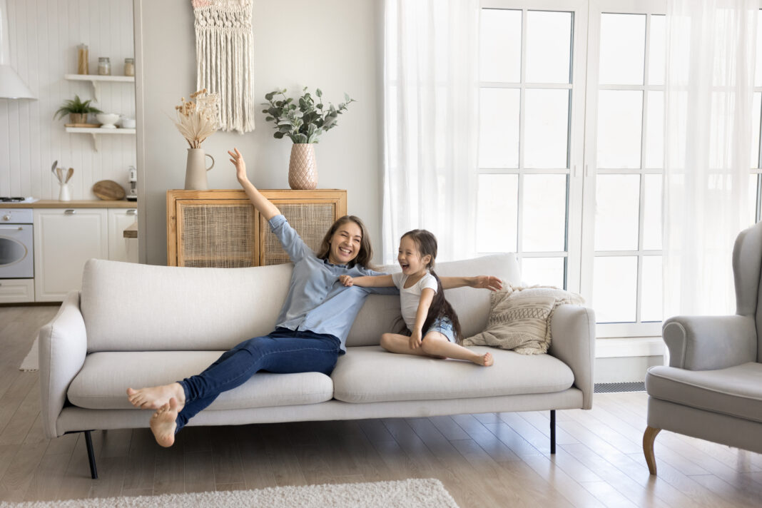 Excited mom little daughter rest on sofa at comfortable home